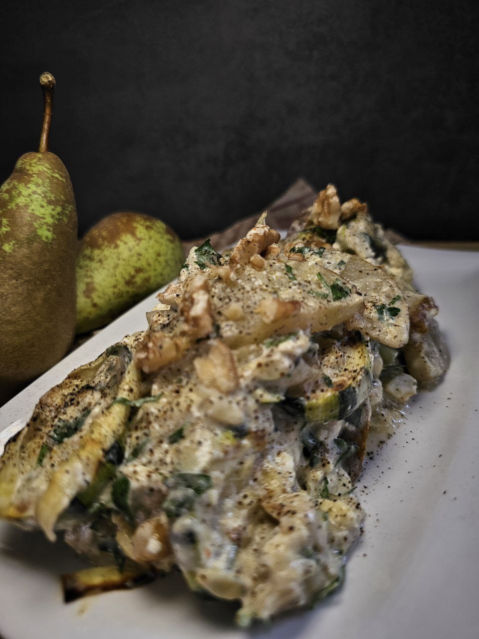 Zucchini-Birnen-Salat mit cremigem Feta-Dressing, serviert auf einem Teller mit frischen Kräutern und Walnüssen.