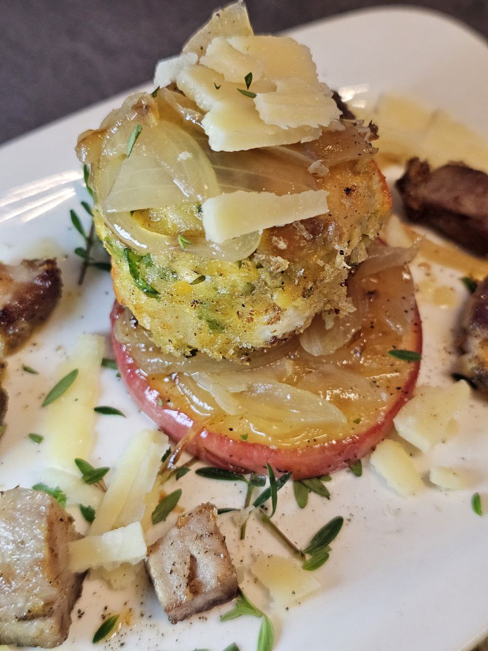 Kürbis Knödel mit Fetakäse und gebratenen Apfelscheiben, angerichtet mit frischem Thymian und Parmesan auf einem rustikalen Teller.