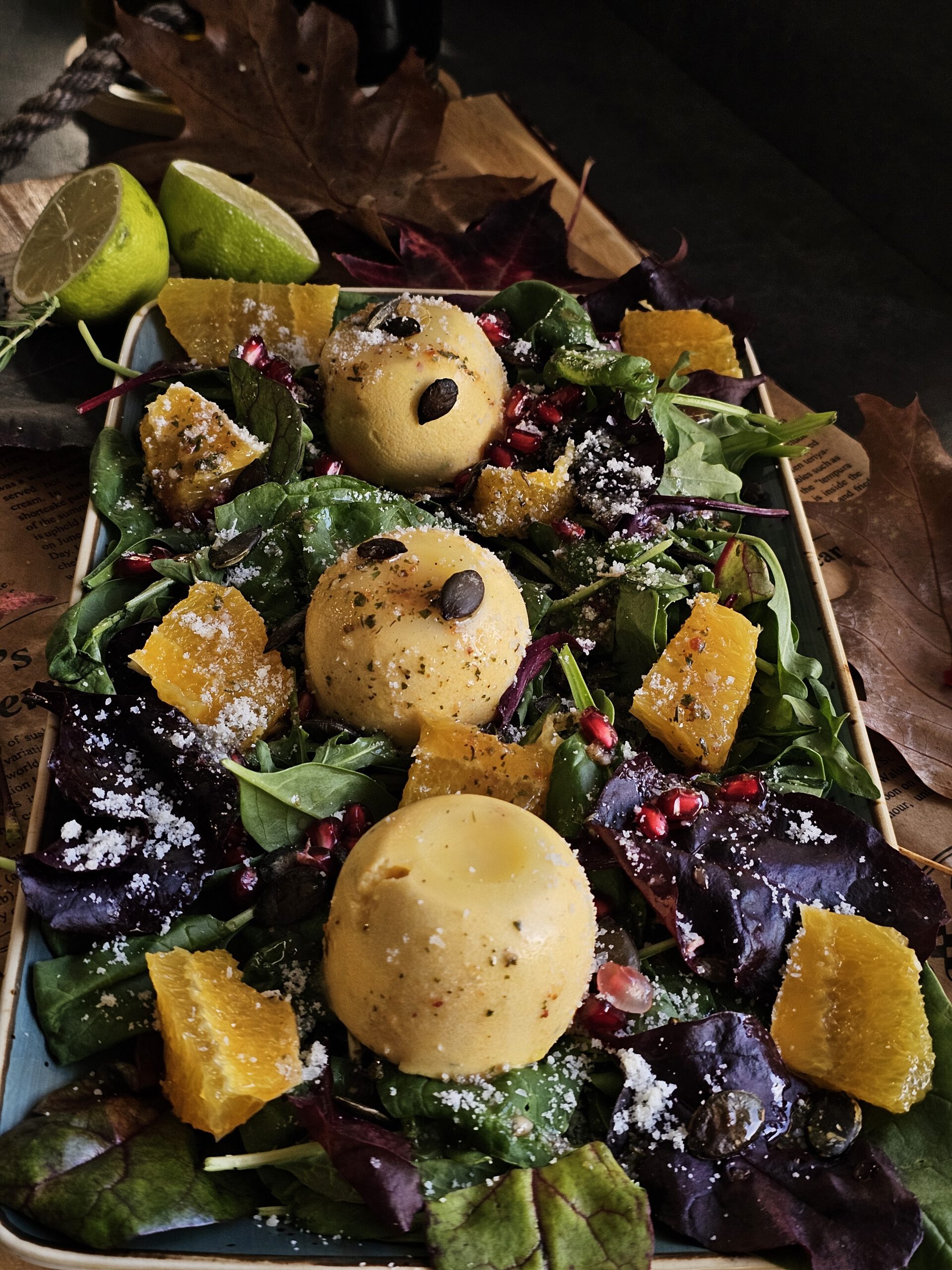 Herzhafte Kürbis Panna Cotta serviert auf einem frischen Herbstsalat mit Orangenfilets, Granatapfelkernen und Kürbiskernen, dekoriert mit geriebenem Parmesan