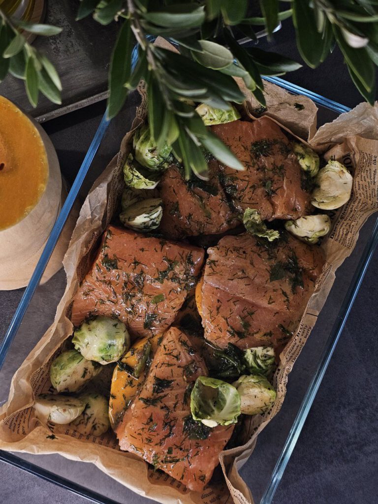 Lachs mit Kürbis in Orangensauce, angerichtet mit Rosenkohl, frischen Kräutern und knusprigen Nüssen – herbstliche Farben auf einem Teller.