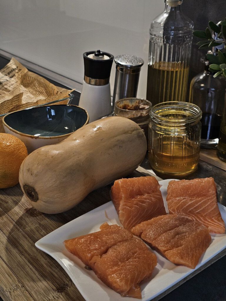 Lachs mit Kürbis in Orangensauce, angerichtet mit Rosenkohl, frischen Kräutern und knusprigen Nüssen – herbstliche Farben auf einem Teller.