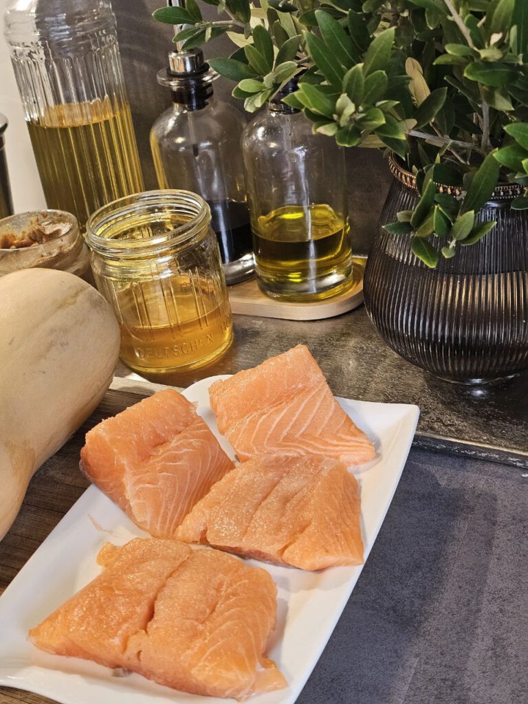 Lachs mit Kürbis in Orangensauce, angerichtet mit Rosenkohl, frischen Kräutern und knusprigen Nüssen – herbstliche Farben auf einem Teller.