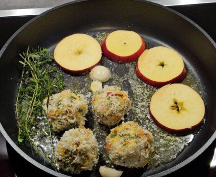 Kürbis Knödel mit Fetakäse und gebratenen Apfelscheiben, angerichtet mit frischem Thymian und Parmesan auf einem rustikalen Teller.