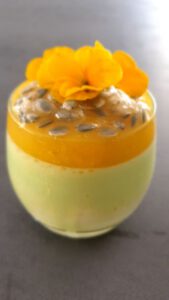 Pistazien-Zitronen Panna Cotta in einem Glas, garniert mit gehackten Pistazien und Zitronenschale.