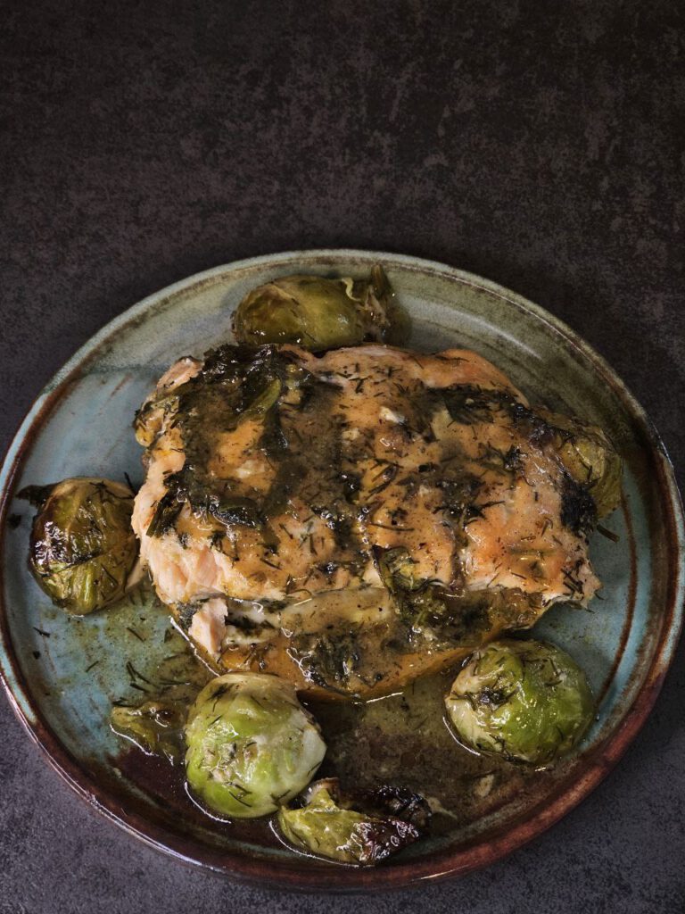 Lachs mit Kürbis in Orangensauce, angerichtet mit Rosenkohl, frischen Kräutern und knusprigen Nüssen – herbstliche Farben auf einem Teller.