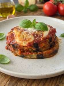 Angerichtetes Stück Parmigiana di Melanzane mit sichtbaren Schichten aus Auberginen, Tomatensauce und Käse