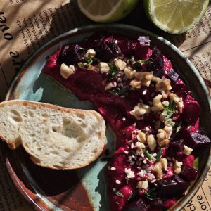 Rote Bete Hummus, ein leuchtend pinker, veganer Dip aus Kichererbsen und Roter Bete, garniert mit frischen Kräutern und Granatapfelkernen.