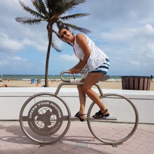 Fahrrad-Skulptur am Strand von Fort Lauderdale, umgeben von Palmen und Blick auf das Meer.