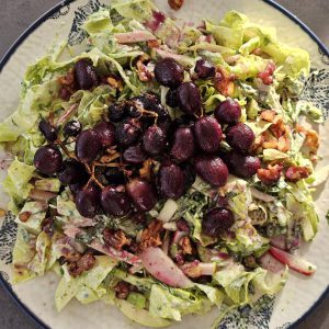 Gegrillter Trauben-Walnuss-Salat mit Estragon-Joghurt-Dressing, garniert mit karamellisierten Trauben und knusprigen Walnüssen, serviert auf einem Bett aus frischem Römersalat, Sellerie, Apfelscheiben und Radieschen.